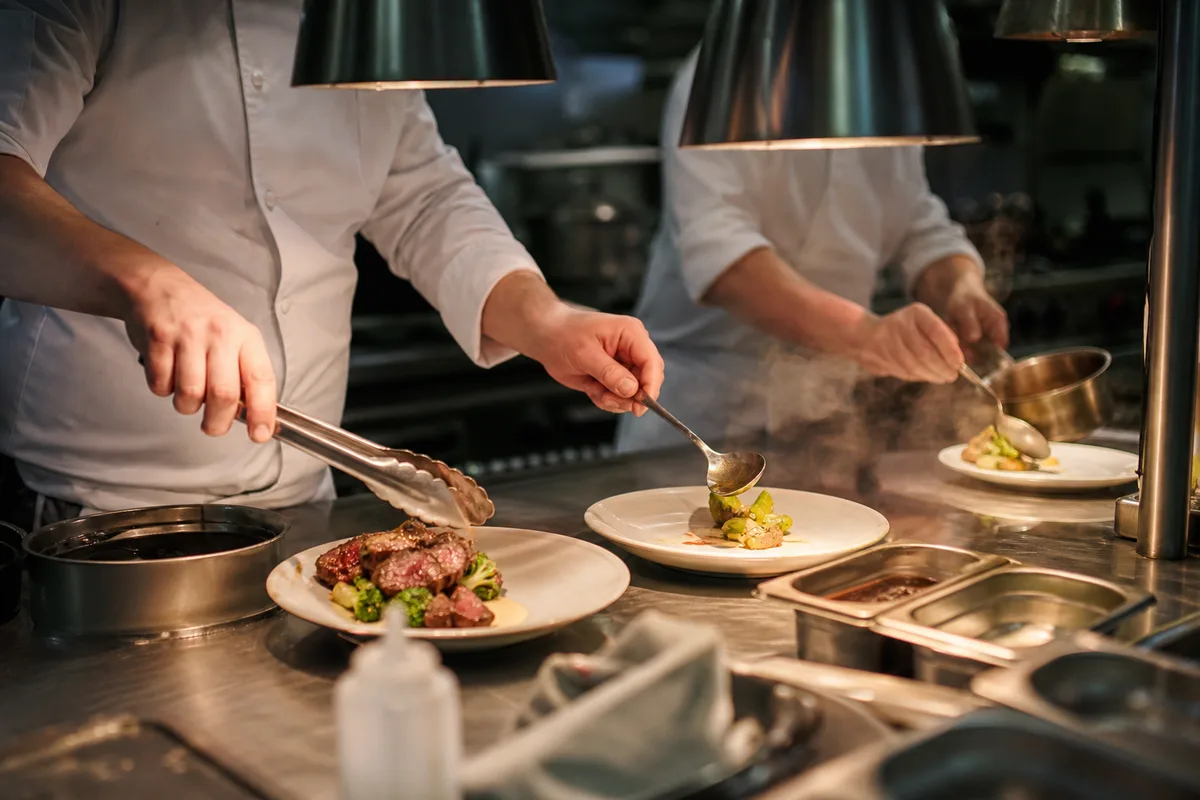 Brigade de cuisine en plein service, dressage d’assiettes sur le passe
